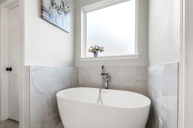 full bathroom with wainscoting, a soaking tub, and tile walls