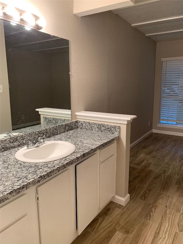 bathroom with a textured wall, vanity, baseboards, and wood finished floors