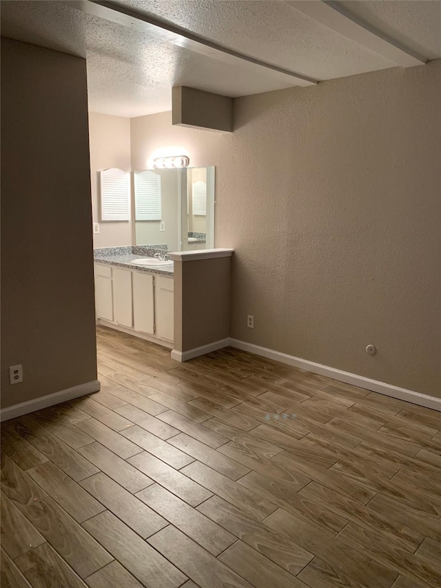 empty room featuring a textured ceiling, a textured wall, a sink, wood finished floors, and baseboards