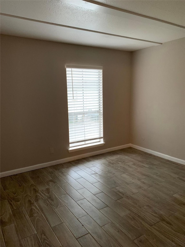 empty room with a textured ceiling, wood finished floors, and baseboards