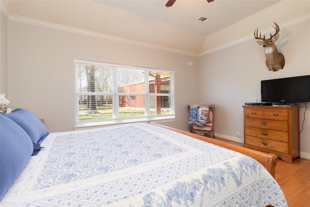 bedroom with lofted ceiling, wood finished floors, visible vents, baseboards, and crown molding