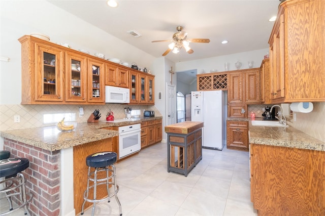 kitchen featuring a breakfast bar area, visible vents, a sink, white appliances, and a peninsula