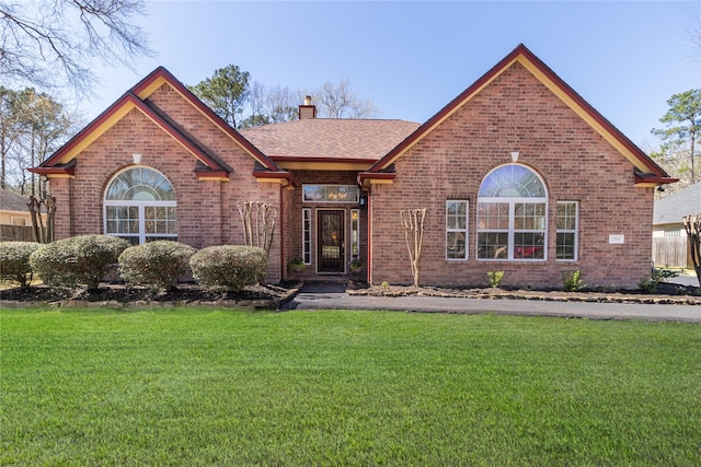 view of front of home with roof with shingles, a front yard, a chimney, and brick siding