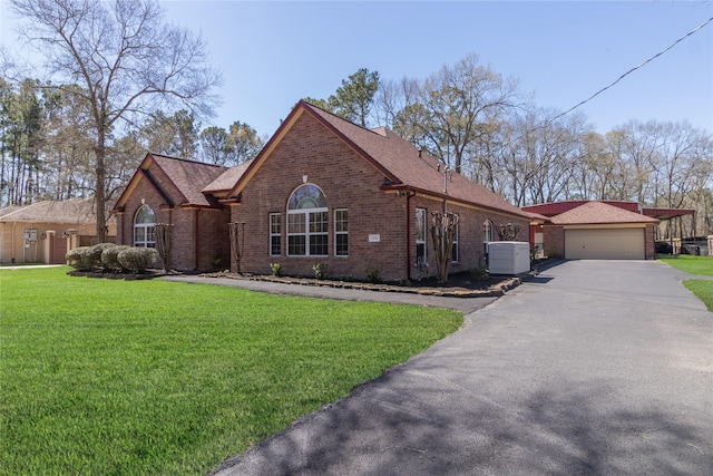 view of front of house featuring brick siding, a detached garage, roof with shingles, a front yard, and cooling unit