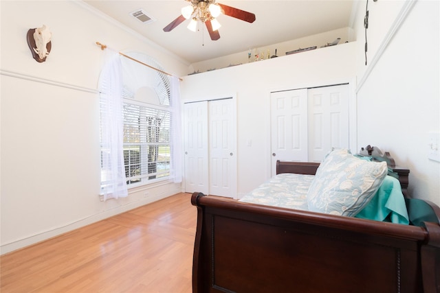 bedroom with ceiling fan, light wood-type flooring, two closets, and visible vents