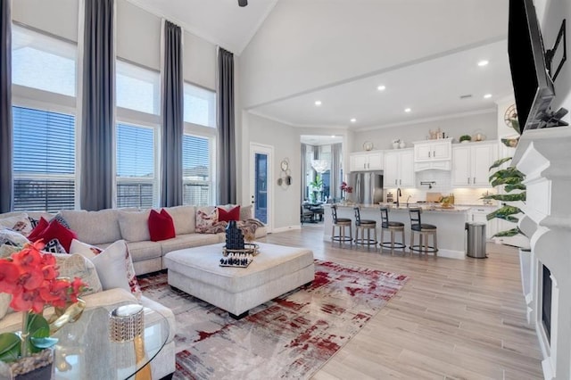 living area featuring a wealth of natural light, high vaulted ceiling, ornamental molding, and light wood-style flooring