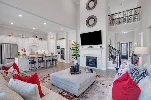 living room featuring ornamental molding, light wood-style flooring, baseboards, and stairs