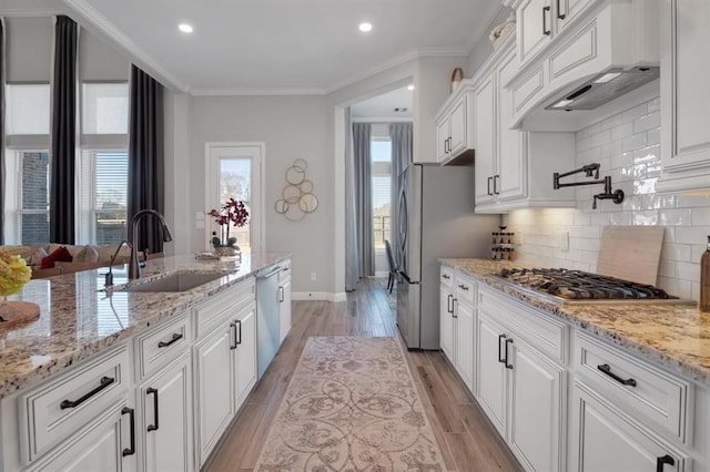 kitchen featuring crown molding, stainless steel appliances, white cabinets, a sink, and light wood-type flooring