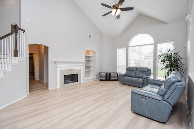 living room featuring built in shelves, arched walkways, light wood finished floors, visible vents, and a tile fireplace