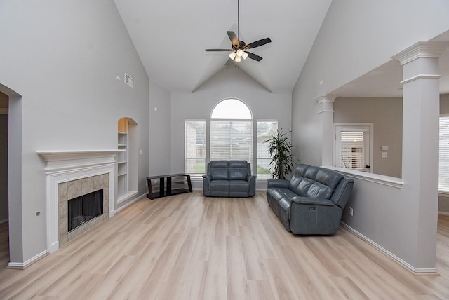 living room featuring a tiled fireplace, ceiling fan, wood finished floors, high vaulted ceiling, and ornate columns