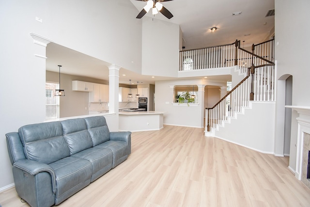 living room featuring stairs, ornate columns, light wood-style flooring, and a ceiling fan