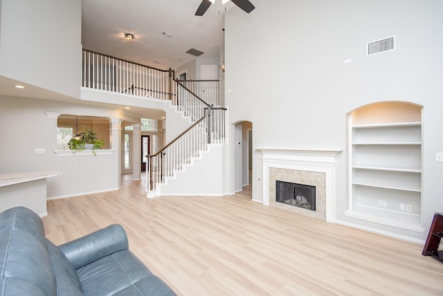 living room featuring built in shelves, a tile fireplace, wood finished floors, visible vents, and stairs