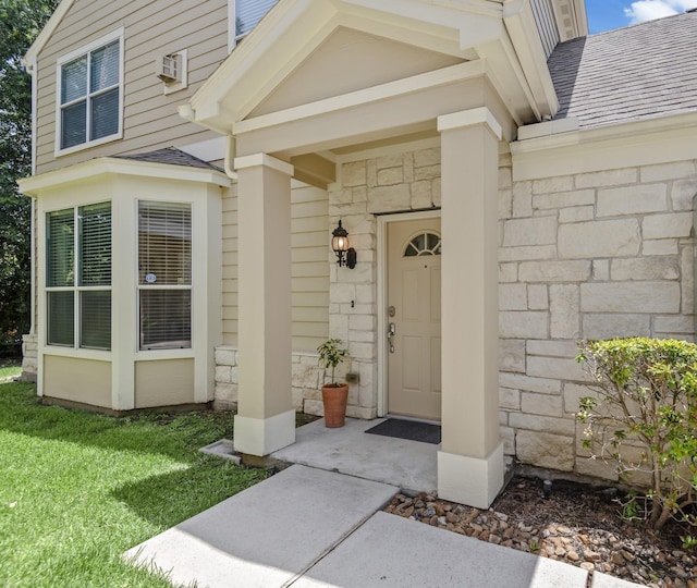 doorway to property featuring stone siding, a yard, roof with shingles, and a wall mounted AC