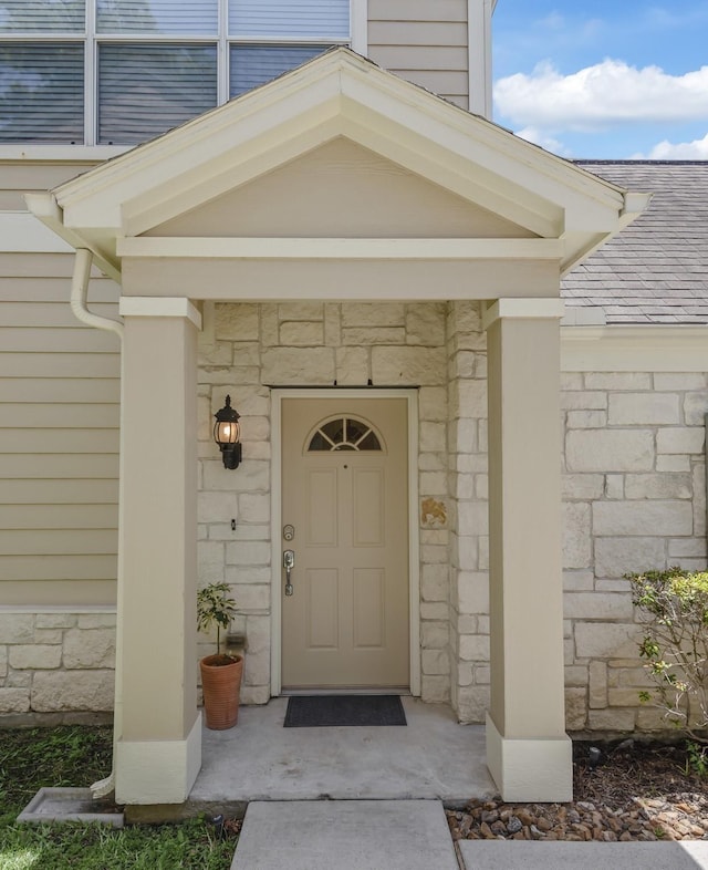 doorway to property with a shingled roof and stone siding