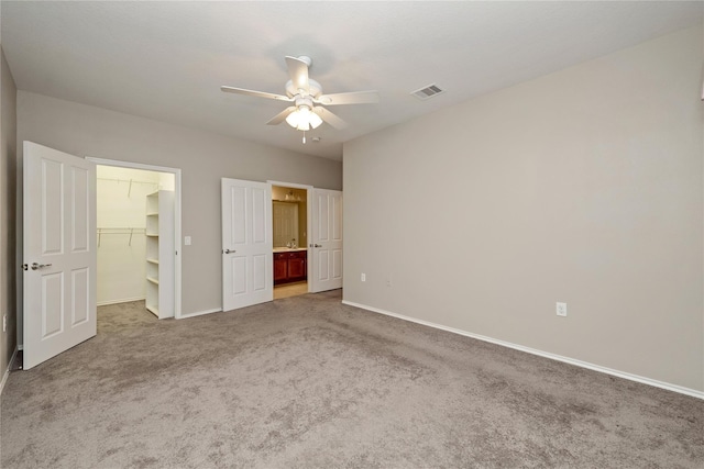 unfurnished bedroom featuring a walk in closet, baseboards, visible vents, and carpet flooring