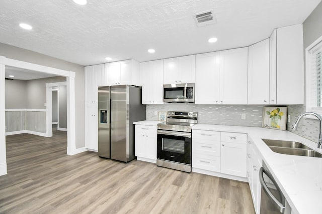 kitchen featuring stainless steel appliances, visible vents, light wood-style flooring, white cabinets, and a sink