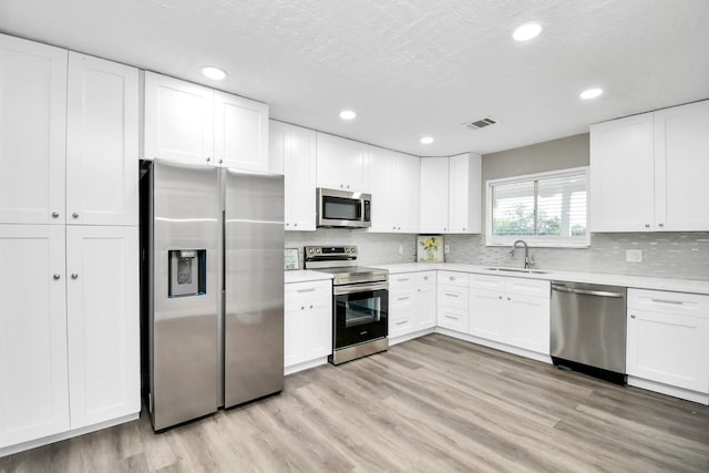 kitchen with stainless steel appliances, light wood finished floors, a sink, and visible vents