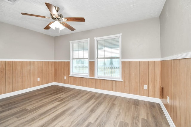 spare room featuring wooden walls, a wainscoted wall, a textured ceiling, and wood finished floors