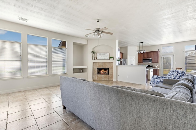 living room featuring baseboards, visible vents, a tiled fireplace, ceiling fan, and light tile patterned flooring