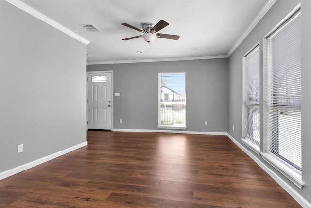 spare room featuring crown molding, dark wood finished floors, visible vents, ceiling fan, and baseboards