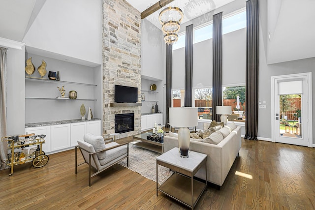 living room with built in shelves, a notable chandelier, a fireplace, dark wood-type flooring, and high vaulted ceiling