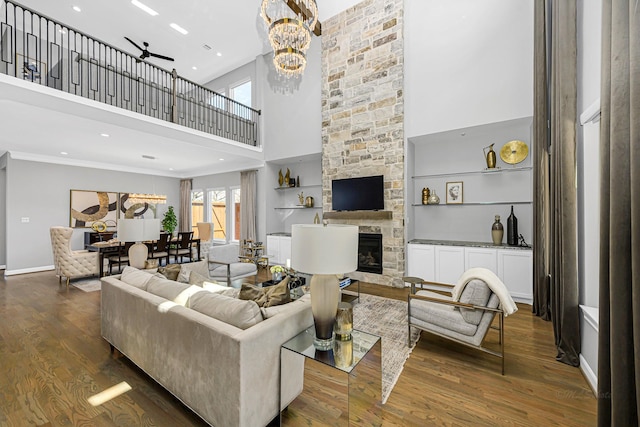 living area featuring baseboards, a towering ceiling, wood finished floors, a fireplace, and a chandelier