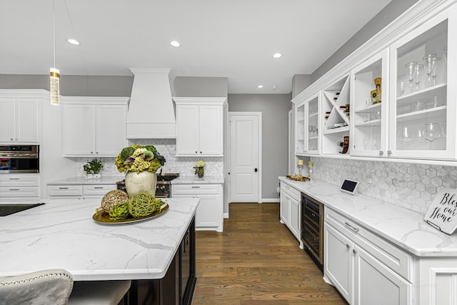 kitchen with wine cooler, glass insert cabinets, custom range hood, stainless steel oven, and white cabinetry