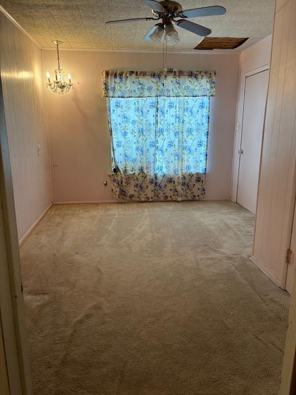 empty room with ceiling fan with notable chandelier, carpet flooring, and wooden walls