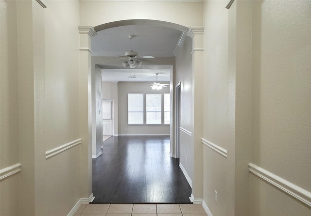 corridor featuring tile patterned floors, crown molding, arched walkways, and baseboards