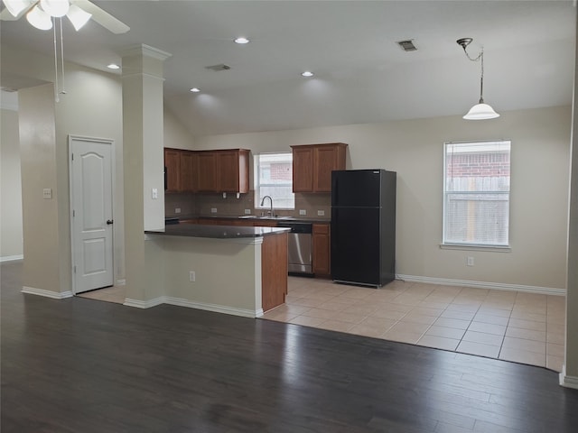 kitchen with stainless steel dishwasher, freestanding refrigerator, vaulted ceiling, a sink, and a peninsula