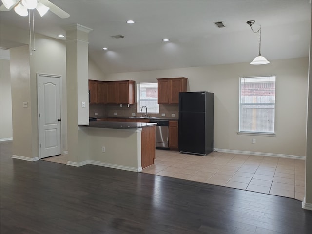 kitchen with a peninsula, lofted ceiling, a sink, stainless steel dishwasher, and freestanding refrigerator