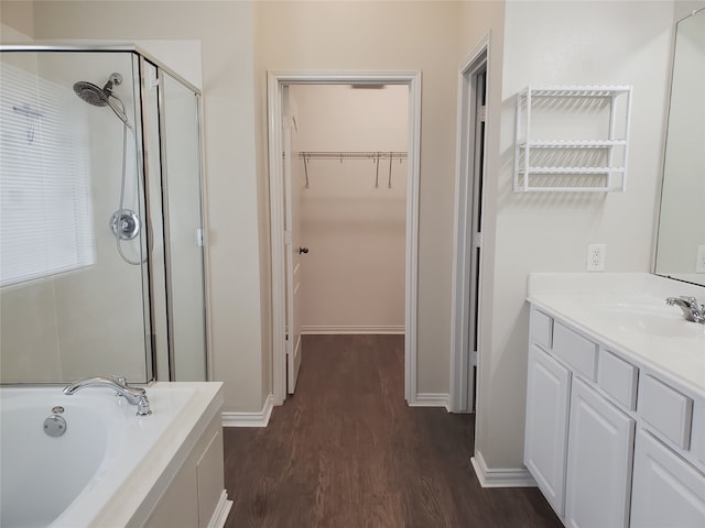 full bath with a spacious closet, a stall shower, vanity, wood finished floors, and a bath