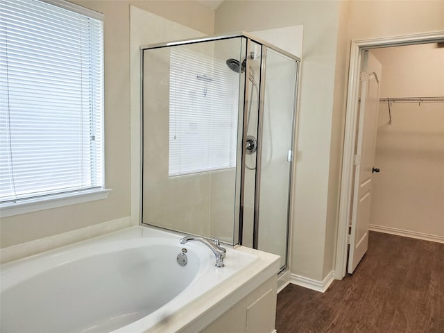 bathroom featuring wood finished floors, a stall shower, a garden tub, and a walk in closet