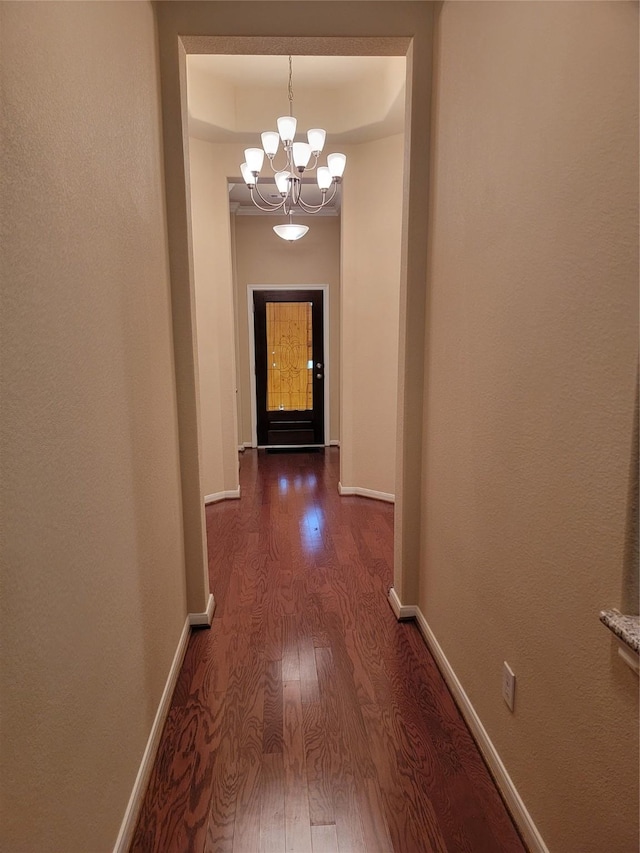 corridor with a tray ceiling, an inviting chandelier, dark wood finished floors, and baseboards