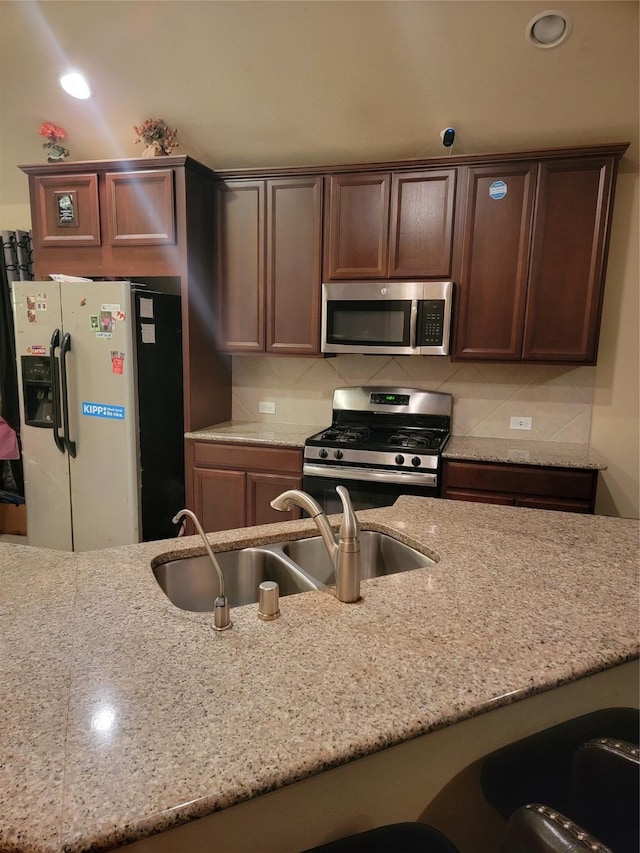 kitchen featuring stainless steel appliances, backsplash, a sink, and light stone countertops