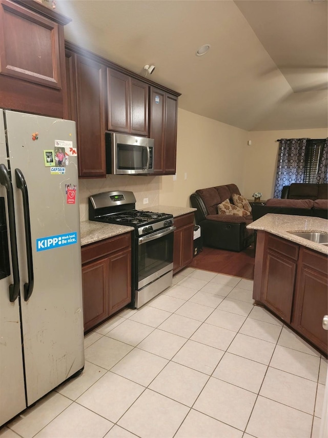 kitchen featuring open floor plan, stainless steel appliances, dark brown cabinets, a sink, and light tile patterned flooring