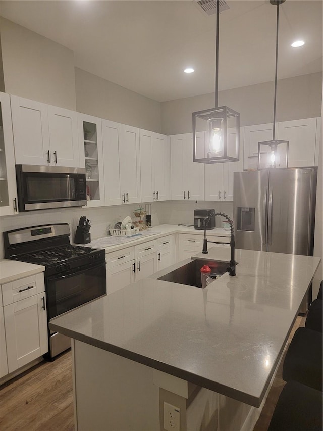 kitchen featuring white cabinets, wood finished floors, stainless steel appliances, a kitchen bar, and a sink