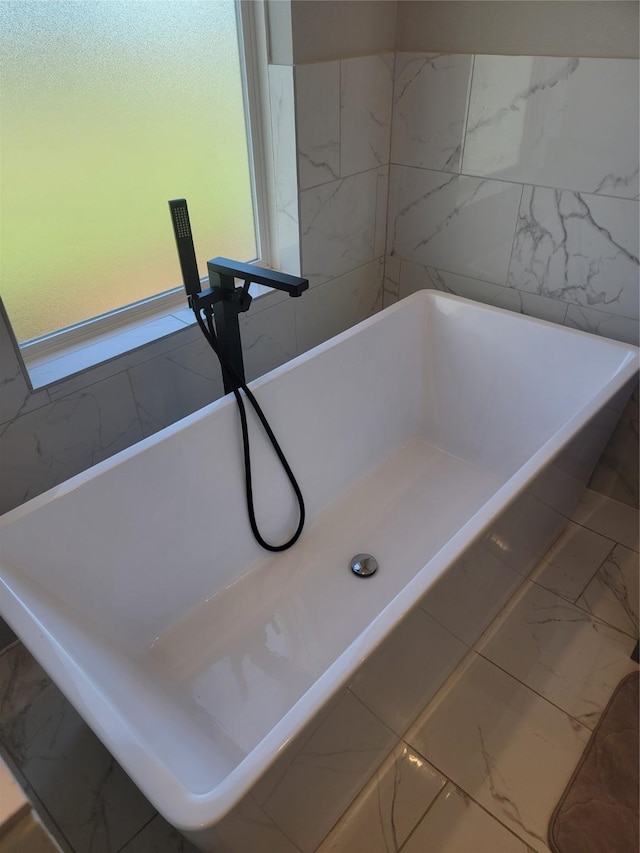 bathroom featuring marble finish floor, a freestanding bath, and a sink