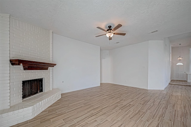 unfurnished living room with a fireplace, visible vents, light wood-style flooring, a ceiling fan, and a textured ceiling