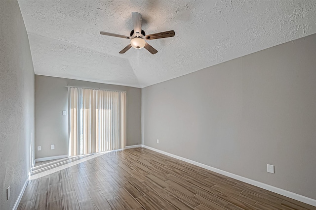 spare room with wood finish floors, vaulted ceiling, ceiling fan, a textured ceiling, and baseboards