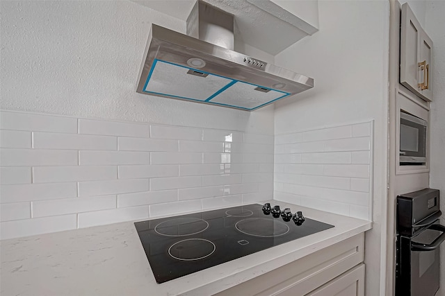 kitchen with wall chimney exhaust hood, black electric stovetop, light stone counters, and stainless steel microwave