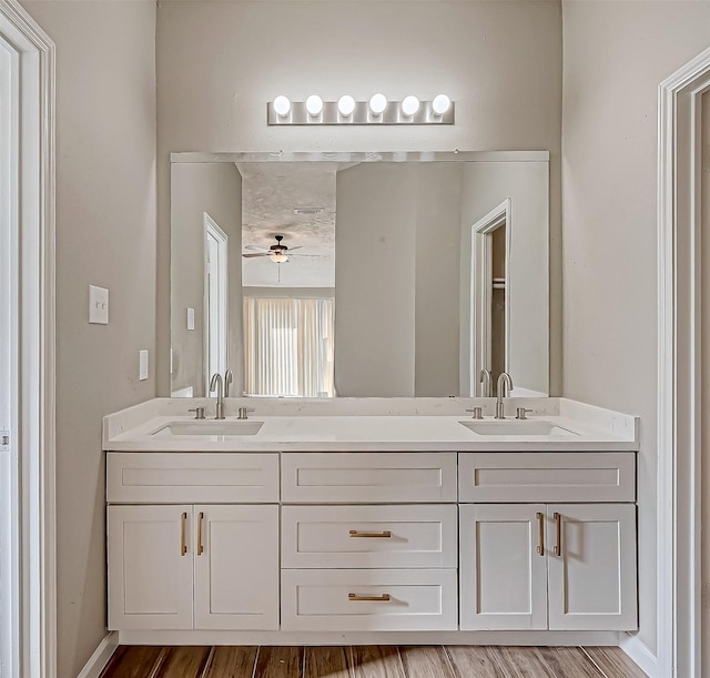 bathroom featuring ceiling fan, wood finished floors, a sink, and double vanity