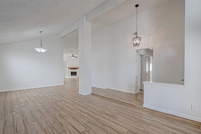 empty room with wood finish floors, a fireplace with raised hearth, a textured ceiling, baseboards, and ceiling fan with notable chandelier