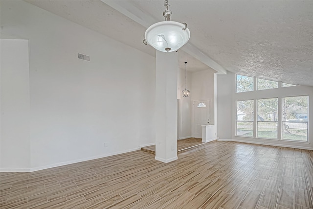 spare room with vaulted ceiling with beams, a textured ceiling, wood finish floors, visible vents, and baseboards