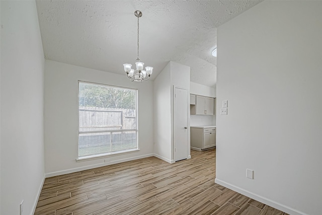 unfurnished dining area with light wood-style flooring, a textured ceiling, baseboards, and a notable chandelier