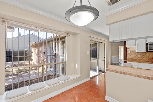 kitchen with light tile patterned floors, white cabinetry, visible vents, stainless steel microwave, and crown molding