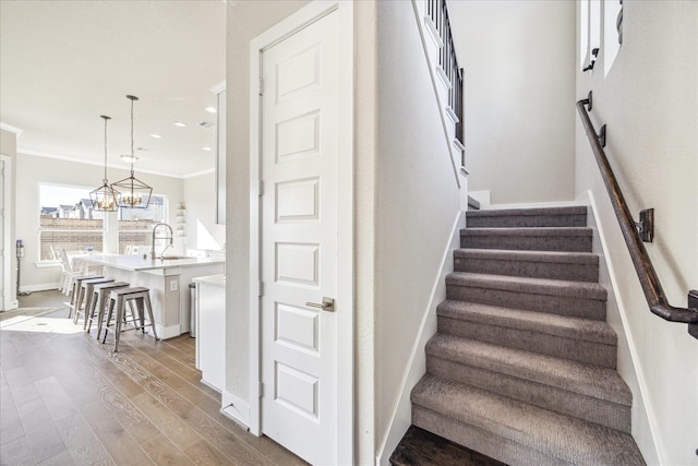 stairway featuring recessed lighting, wood finished floors, baseboards, ornamental molding, and an inviting chandelier