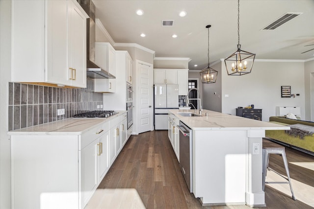 kitchen with wall chimney range hood, appliances with stainless steel finishes, a sink, and visible vents