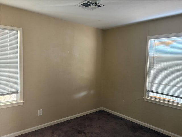 empty room with dark colored carpet, visible vents, and baseboards