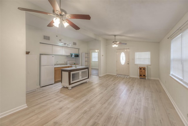 kitchen featuring visible vents, stainless steel microwave, freestanding refrigerator, vaulted ceiling, and light wood-style floors